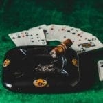 poker csrds and ashtray with brown cigar placed on a green poker table